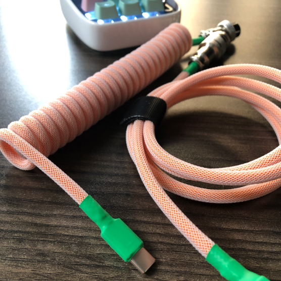 Closeup of a Coiled USB-C power cable on a wooden table with a tiny computer in the background.