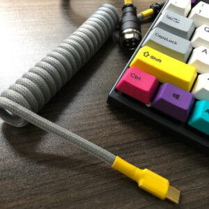 Grey coiled USB cable with yellow ends beside a mechanical keyboard with colourful keycaps