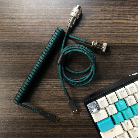 Picture of a green coiled USB cable with the corner of a keyboard displayed on a wooden desk